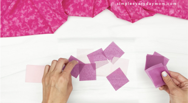 hand placing purple tissue paper squares onto contact paper
