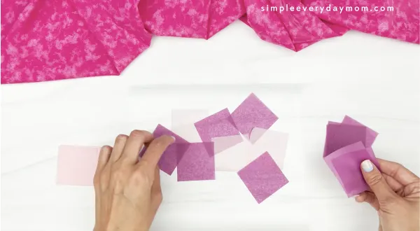 hand placing purple tissue paper squares onto contact paper