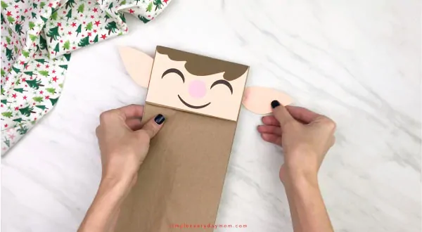 hand gluing ears to paper bag elf craft