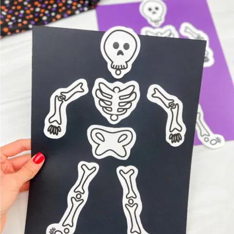 hand holding skeleton paper craft with a second craft in the background