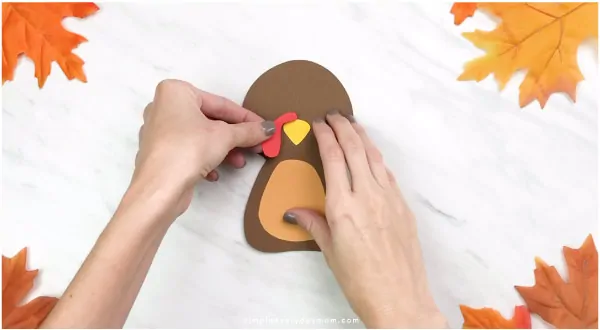 Hands gluing snood onto handprint turkey craft