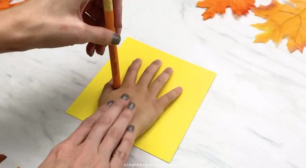 Adult hand tracing child hand on yellow paper