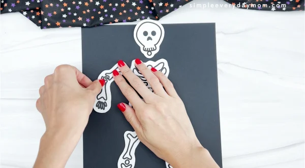 hands gluing skeleton arm to black paper