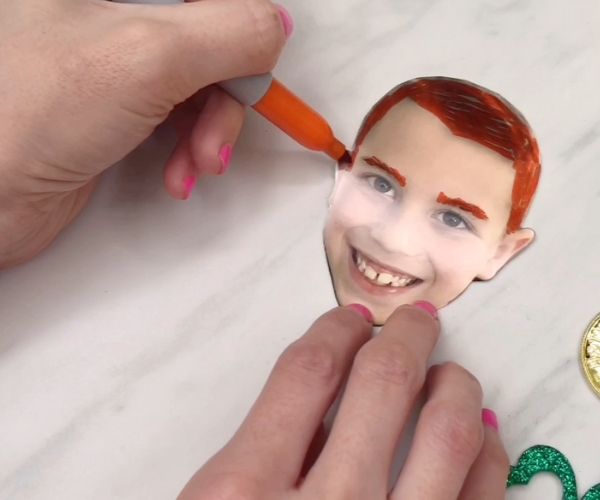 Hand drawing orange hair and eyebrows on boy’s photo 