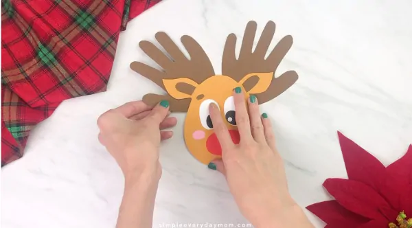 Hands gluing handprint antlers onto handprint reindeer craft 