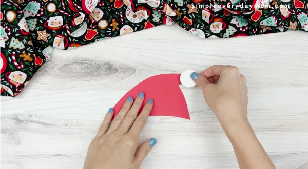 hand gluing hat pom to hat of Santa handprint craft