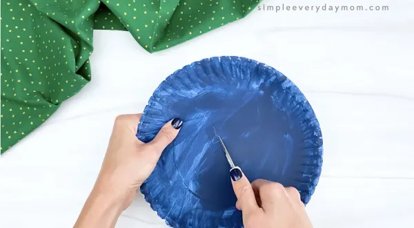hand cutting slit in middle of blue paper plate