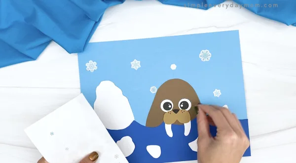 hand putting snowflake stickers onto walrus paper craft