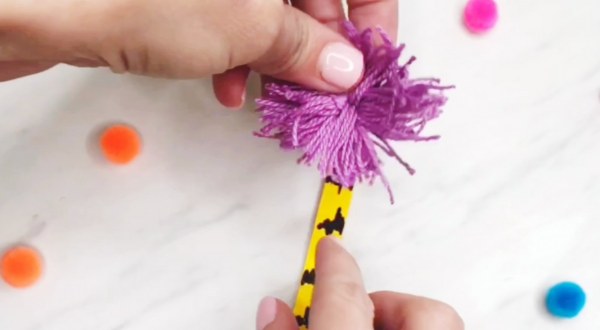 hand gluing embroidery floss pom to popsicle stick