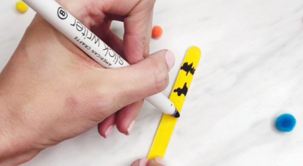 hand drawing wavy lines along yellow popsicle stick 