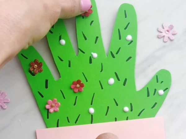 hand gluing mini flower embellishments of Handprint Cactus Mother's Day Card Craft