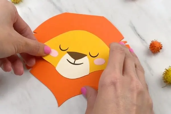 hands gluing on cheeks on paper lion craft