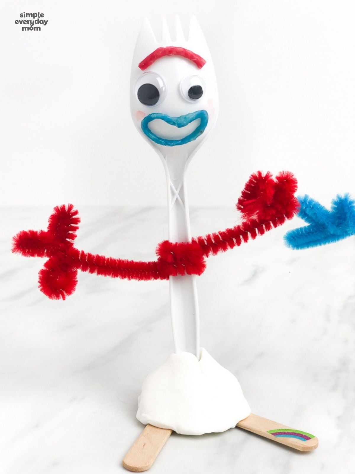 Finished Forky craft with red pipe-cleaner arms, googly eyes, a blue mouth, clay base, and craft-stick feet.