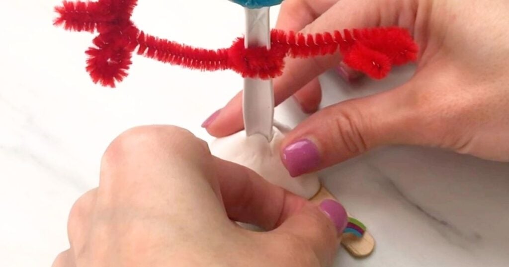 Hands pressing the Forky craft and its craft-stick feet into the clay base.