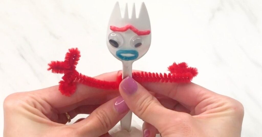 Hands wrapping red pipe-cleaner arms around the handle of the Forky craft.