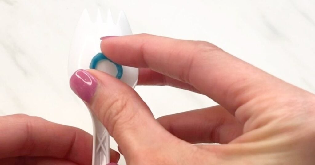 Hand attaching a blue wax stick mouth to the bowl of a plastic fork.