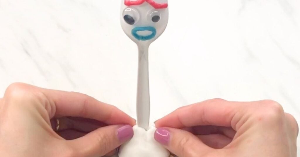 Hands shaping white clay around the base of the plastic fork.