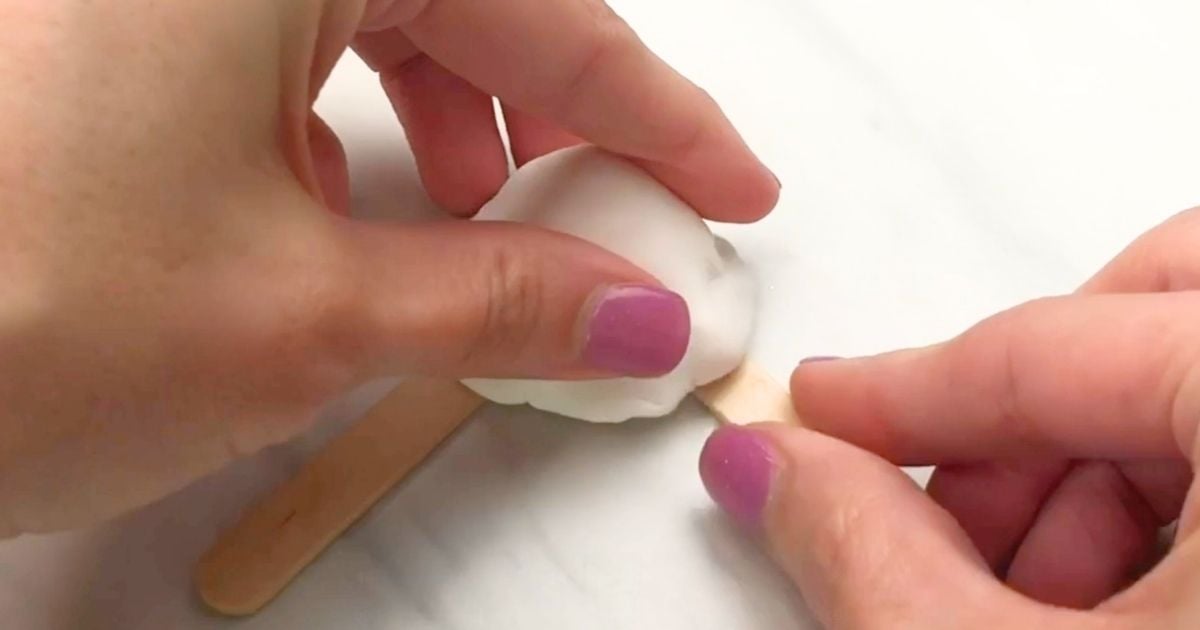 Hands pressing a craft-stick foot into the clay base of a Forky craft.