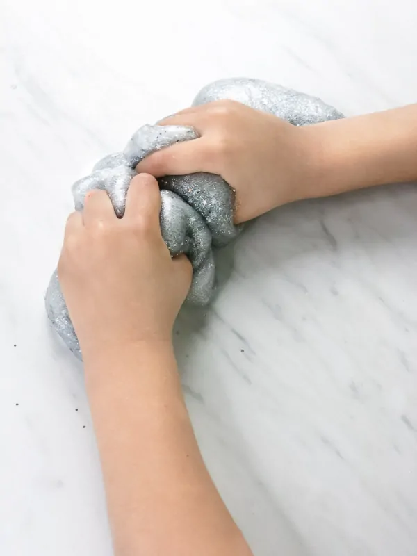 little kids hand squeezing silver slime