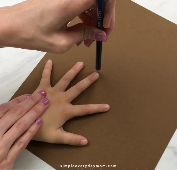 adult hand tracing child's hand on brown paper