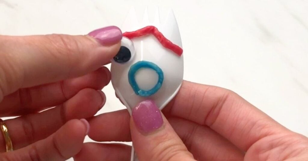 Hand attaching a googly eye to the Forky craft’s face.