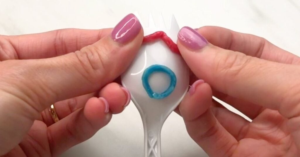 Hands placing a red wikki stix eyebrow across the top of the plastic fork.
