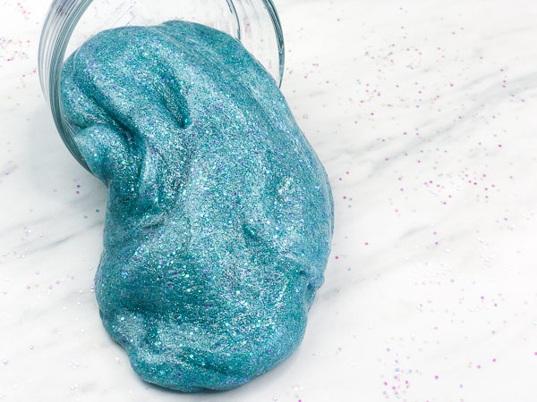teal glitter slime oozing out of clear bowl
