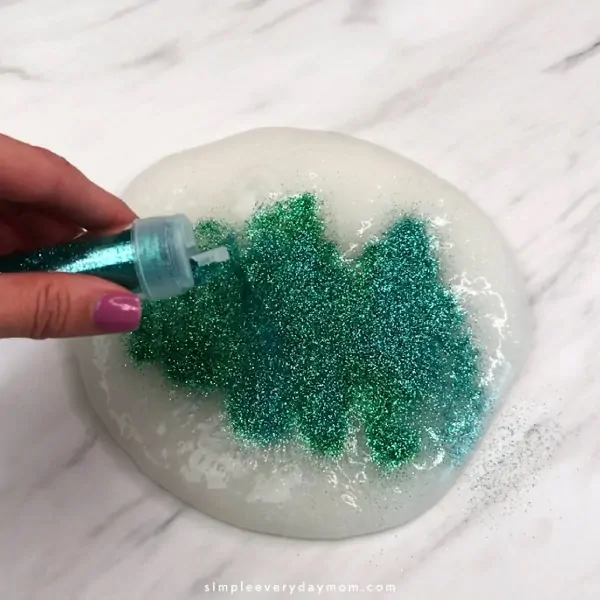 hand pouring green glitter onto clear slime