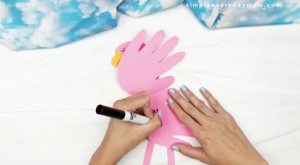 hand writing a message inside flamingo handprint craft