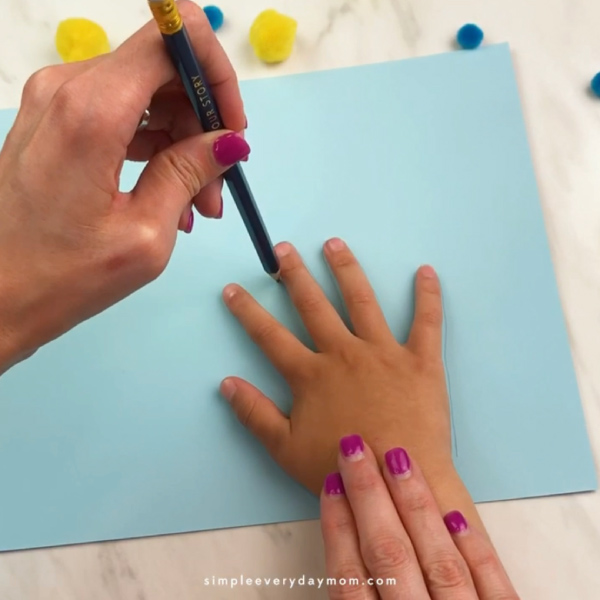 adult hand tracing small child's hand onto light blue paper 
