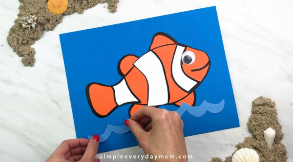 hands gluing paper water to the backdrop for clownfish craft
