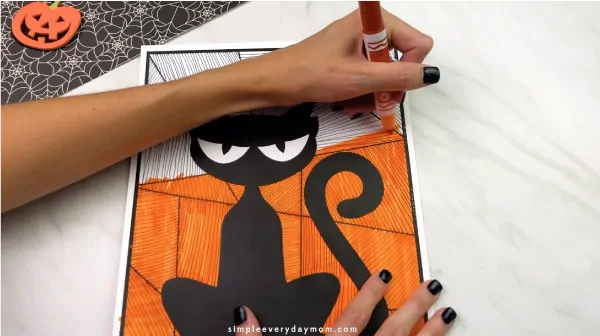 hands using orange marker to color in black cat craft