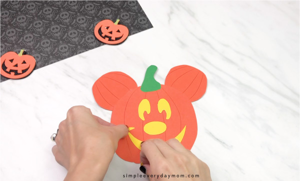 hands gluing mouth onto pumpkin