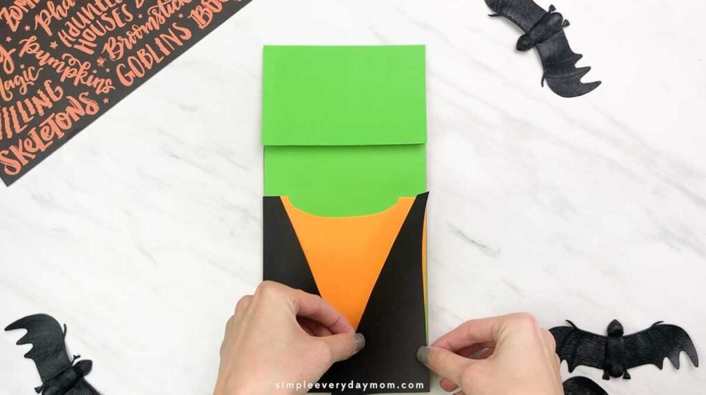 Hands attach black paper jacket pieces over the orange shirt on the Frankenstein puppet.