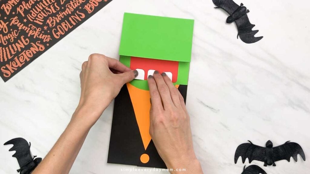 Hands attach white paper teeth inside the red mouth of the Frankenstein puppet.