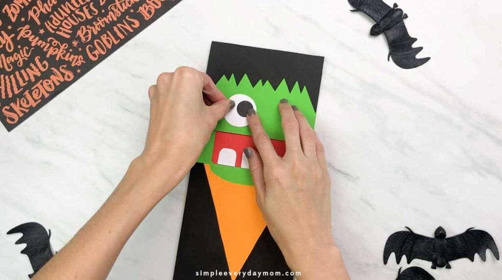Hands attach a large white-and-black paper eye to the Frankenstein puppet’s face.