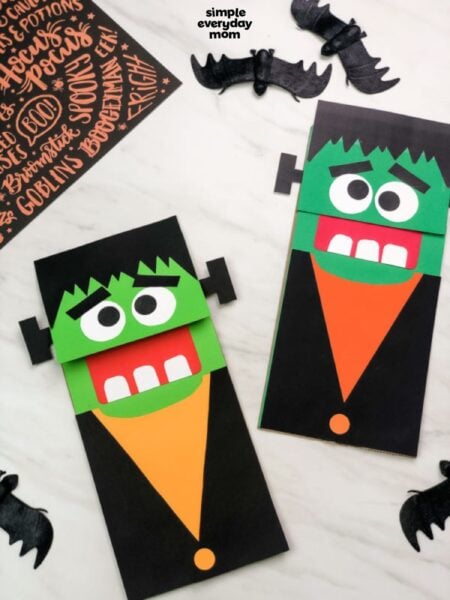 Two finished Frankenstein paper bag puppets displayed with black bat decorations on a light background.