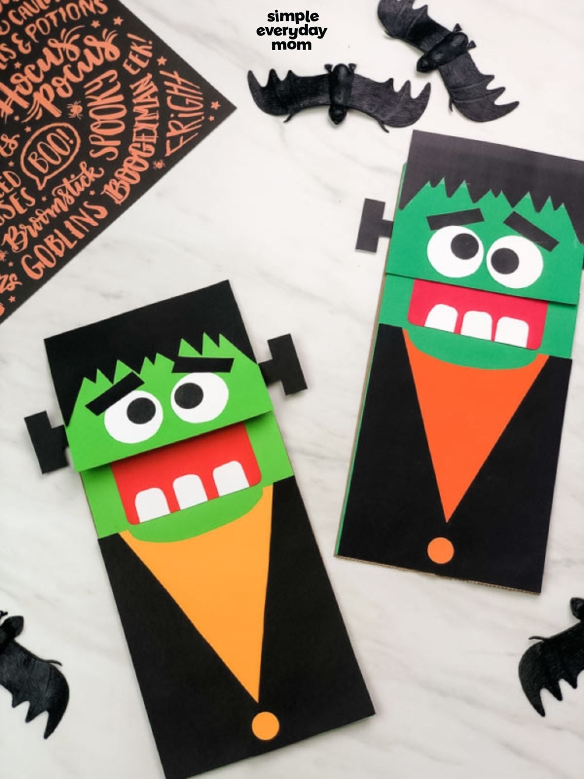 Two finished Frankenstein paper bag puppets displayed with black bat decorations on a light background.