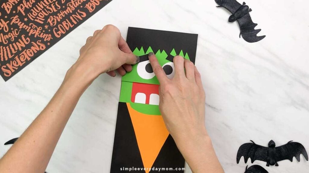 Hands position a black paper eyebrow above the puppet’s eyes.