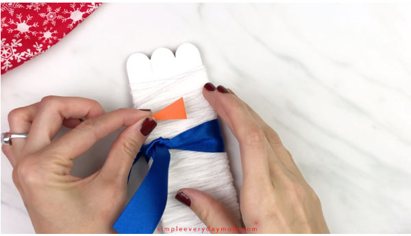Hands gluing nose on popsicle stick snowman 