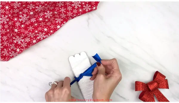 Hands tying bow on popsicle stick snowman 