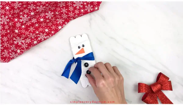 Hands gluing buttons on popsicle stick snowman 