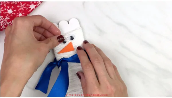 Hands gluing eyes on popsicle stick snowman 
