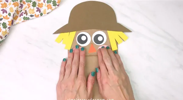 hands gluing cheeks onto paper bag scarecrow