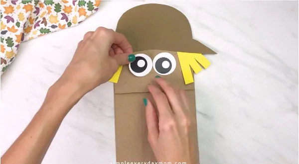 hands gluing eyes onto paper bag scarecrow