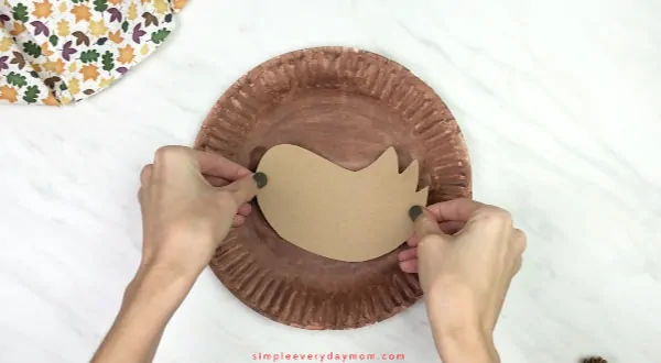 hands gluing wing onto paper plate turkey craft