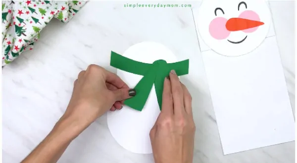 Hands gluing scarf onto paper bag snowman body 