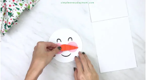 Hands gluing carrot nose on paper bag snowman craft