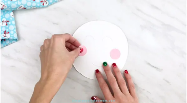 Hands gluing cheeks onto paper plate snowman head