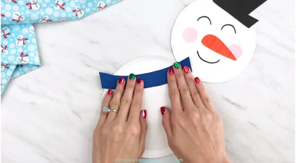 Hands gluing scarf onto paper plate snowman 